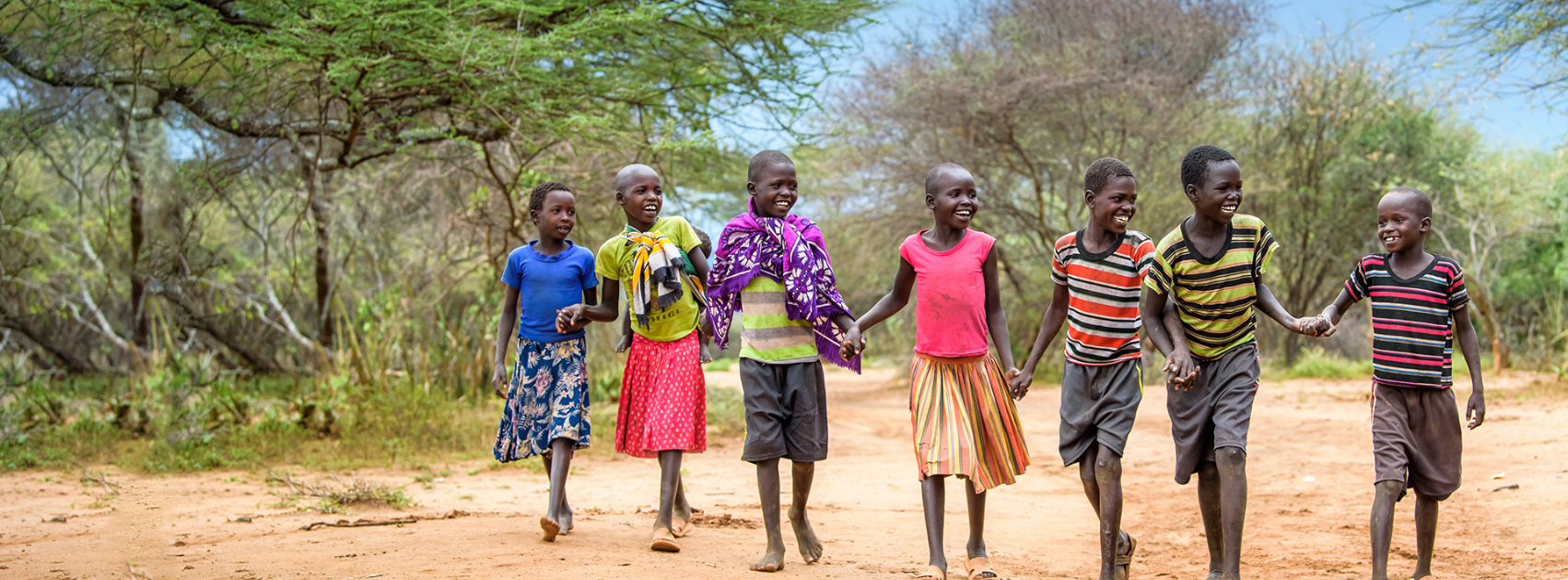 Children walking together hand in hand along a dirt path in a rural community